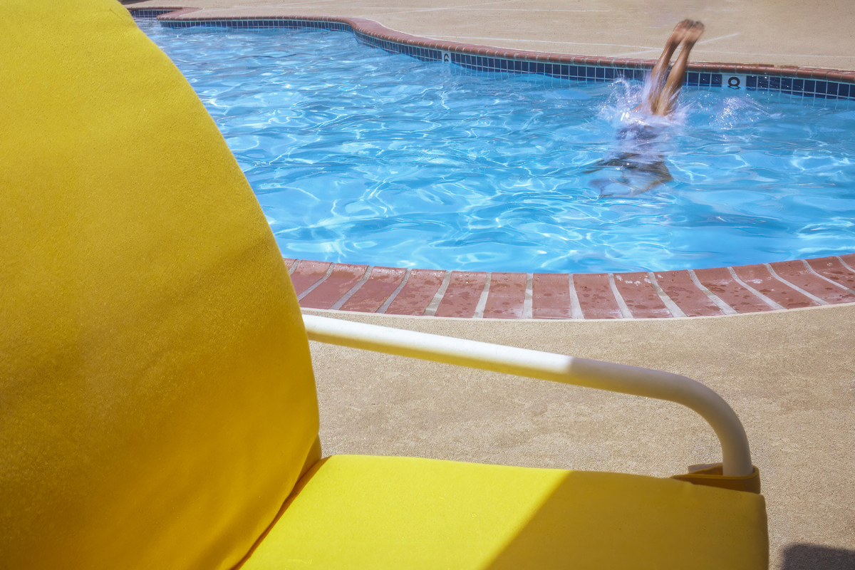 Color photo of a swimming pool with a person diving in to the water with feet showing and a small splash